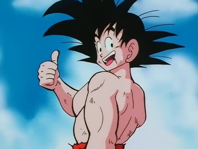 Goku, personaje de anime con cabello negro puntiagudo, sin camiseta, levantando el pulgar en señal de aprobación mientras sonríe.